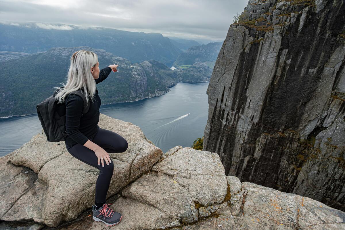 Une femme observe un paysage norvégien et pointe du doigt un point. Montagnes et rivière, elle est en haut d'un sommet