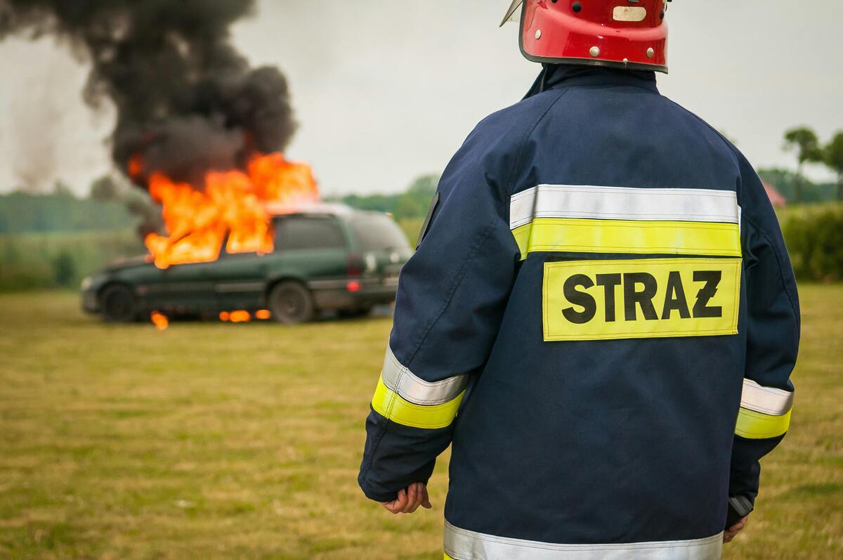 Un pompier qui regarde un véhicule en feu en arrière plan